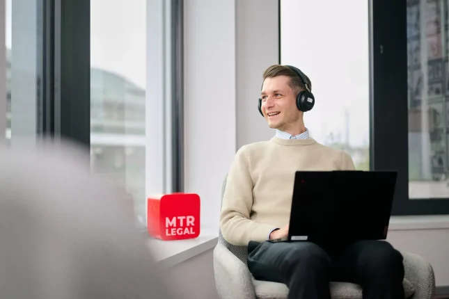 Kollege mit Headset arbeitet im Sessel, daneben der rote MTR-LEGAL-Würfel