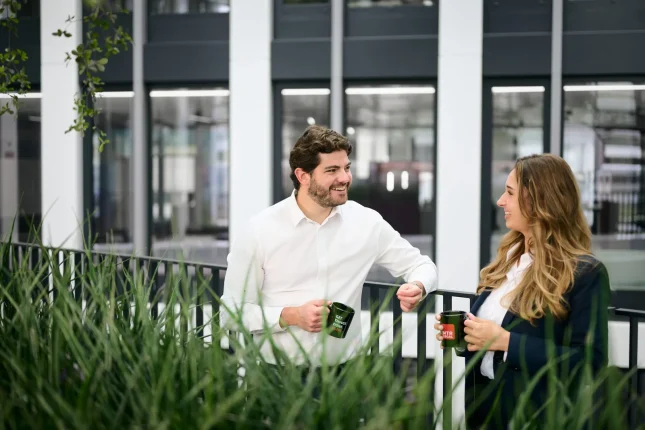 Zwei Kollegen mit Kaffeetassen am Geländer der Dachterrasse