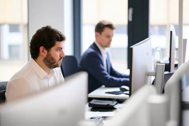 Zwei Kollegen arbeiten konzentriert an ihren Bildschirmen im offenen Bürobereich
