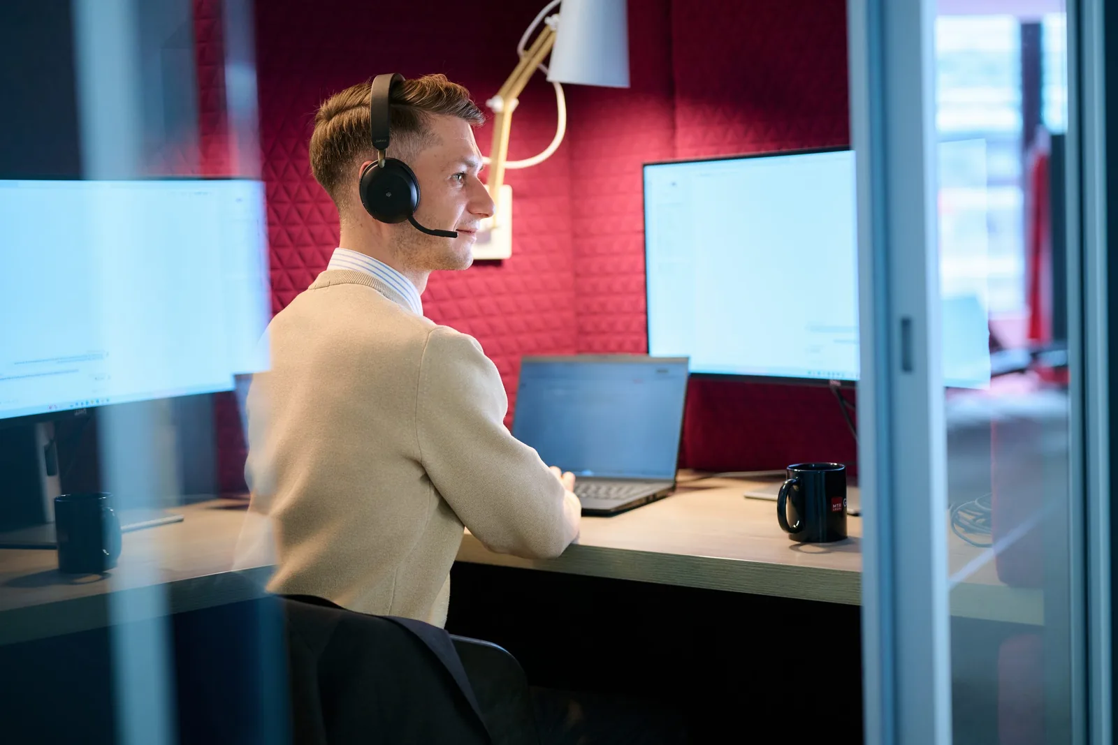 Kollege mit Headset arbeitet in der Telefonbox an zwei Bildschirmen