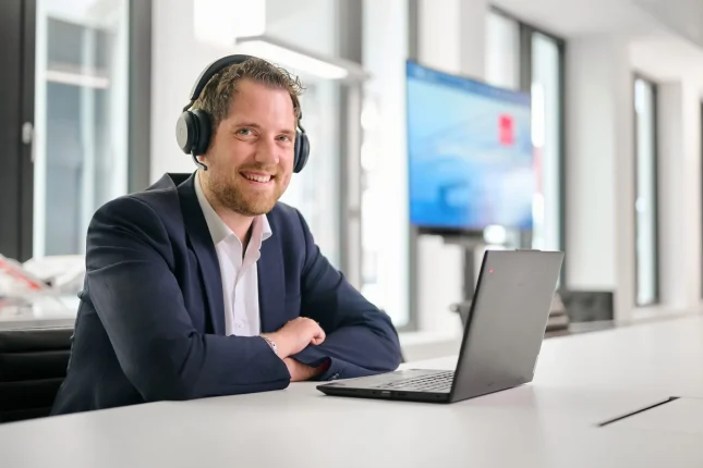Kollege mit Headset am Laptop, lachend während eines Gesprächs