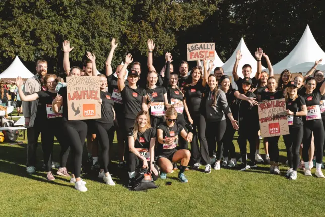 Gruppe in schwarzen Laufshirts mit Startnummern jubelt mit erhobenen Armen und selbst gemalten Schildern