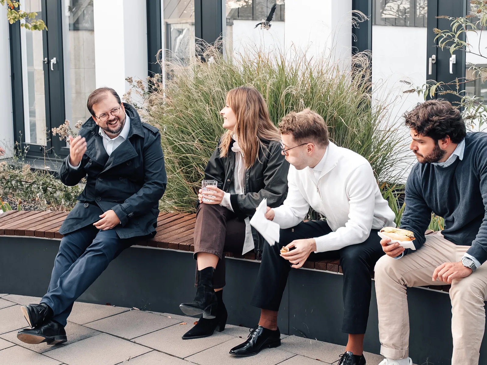 Kolleginnen und Kollegen sitzen auf einer Bank auf der begrünten Dachterrasse und unterhalten sich